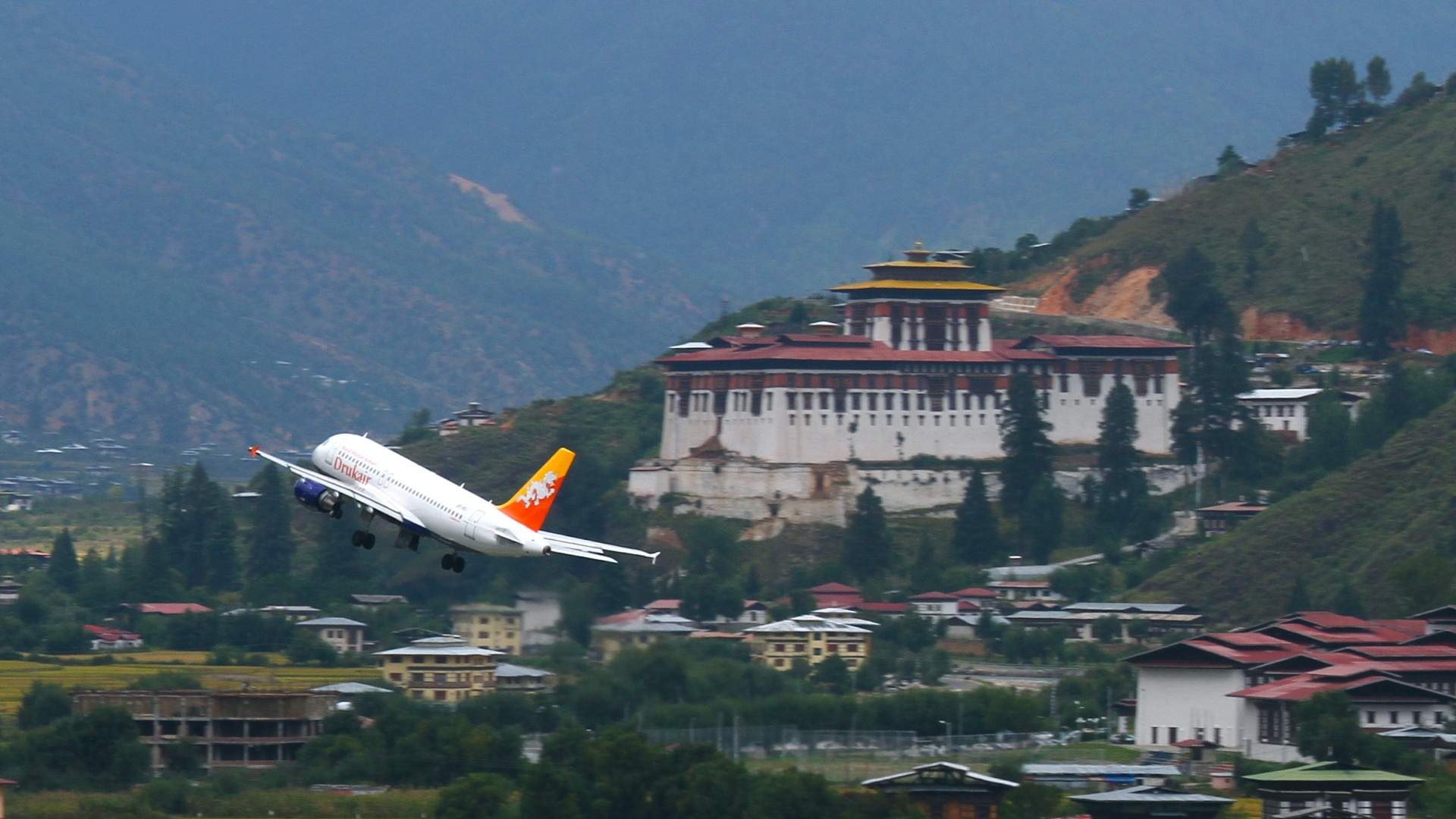 A Drukair jet climbing away from Paro past Rinpung Dzong